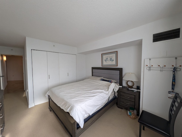 bedroom featuring light colored carpet, a textured ceiling, and a closet