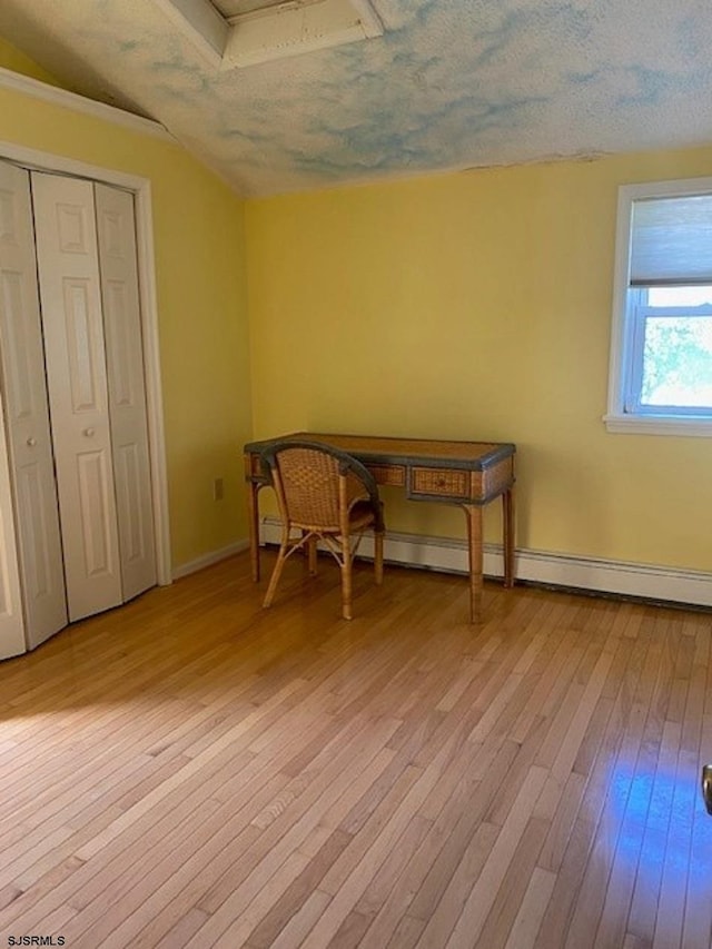 unfurnished room featuring a textured ceiling, a baseboard radiator, and light hardwood / wood-style flooring