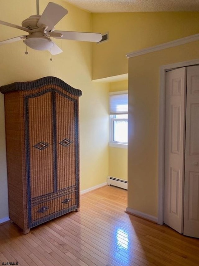 unfurnished bedroom with ceiling fan, baseboard heating, light hardwood / wood-style floors, a textured ceiling, and vaulted ceiling