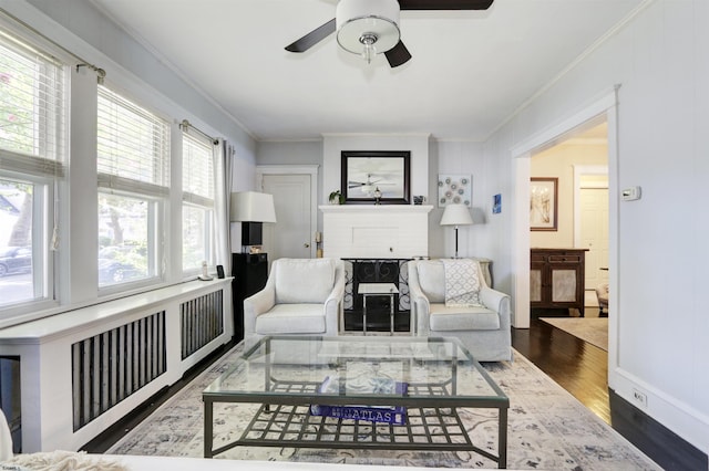 living room featuring hardwood / wood-style flooring, ceiling fan, ornamental molding, and a brick fireplace