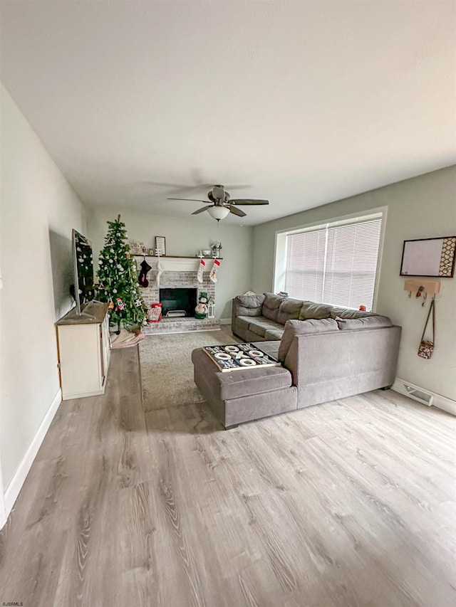 living room featuring light hardwood / wood-style floors, a stone fireplace, and ceiling fan