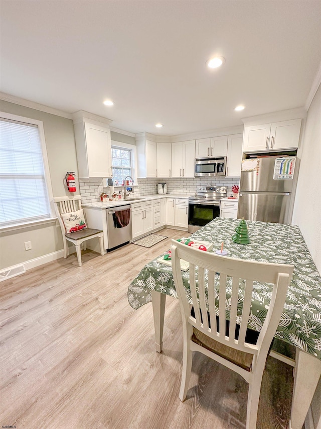 kitchen featuring white cabinets, stainless steel appliances, light wood-type flooring, and ornamental molding