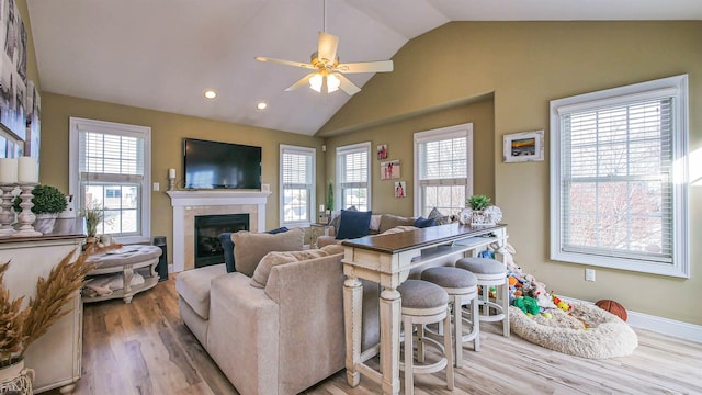 living room with ceiling fan, light hardwood / wood-style floors, a wealth of natural light, and a tiled fireplace