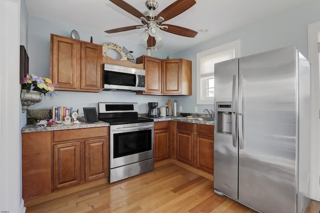 kitchen with light wood-type flooring, light stone counters, stainless steel appliances, ceiling fan, and sink