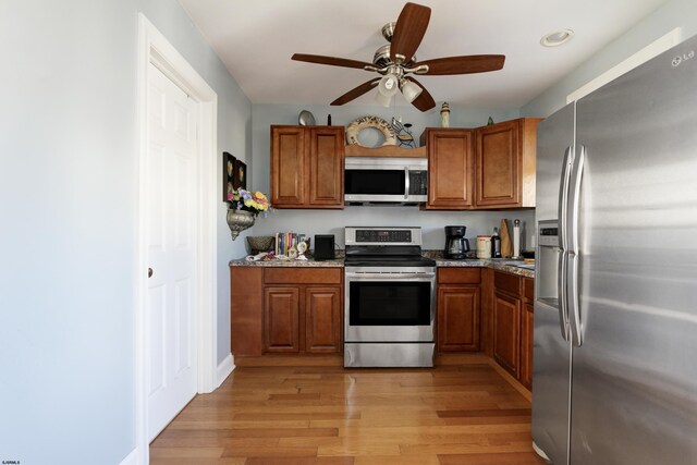 kitchen featuring light stone countertops, ceiling fan, light wood-type flooring, and appliances with stainless steel finishes