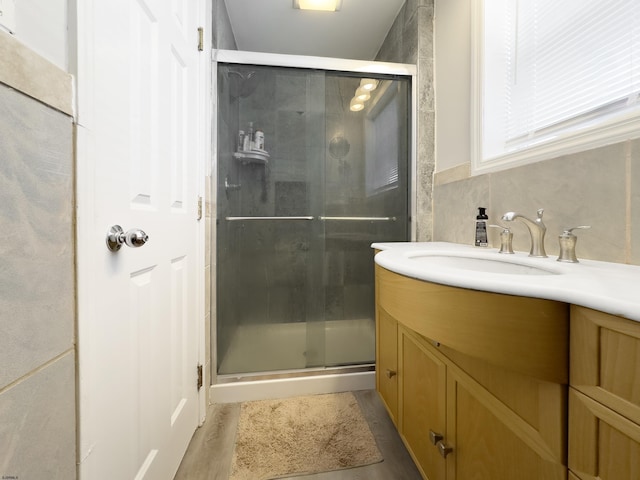 bathroom with hardwood / wood-style flooring, vanity, a shower with shower door, and tile walls