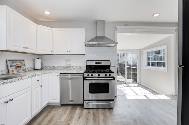 kitchen with light wood-type flooring, tasteful backsplash, wall chimney exhaust hood, stainless steel appliances, and white cabinets