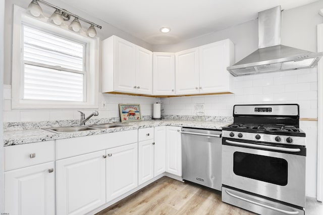 kitchen featuring white cabinets, sink, light hardwood / wood-style flooring, wall chimney exhaust hood, and stainless steel appliances