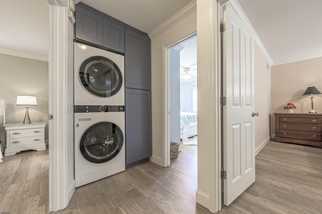 clothes washing area featuring stacked washer / dryer, crown molding, cabinets, and hardwood / wood-style flooring