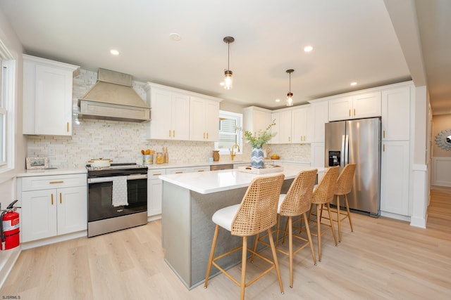 kitchen with custom range hood, stainless steel appliances, white cabinetry, and decorative light fixtures