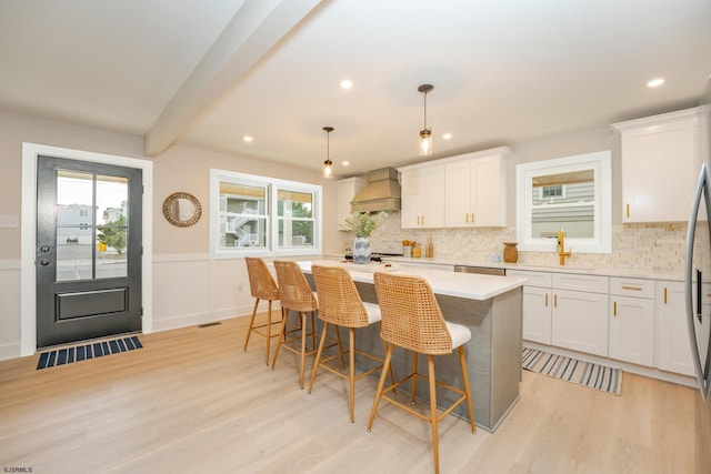 kitchen with a center island, light hardwood / wood-style flooring, decorative light fixtures, white cabinetry, and custom range hood