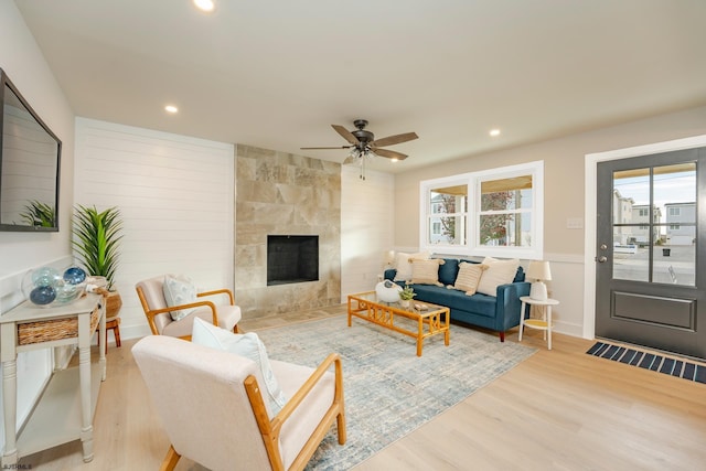 living room with a fireplace, light wood-type flooring, and ceiling fan