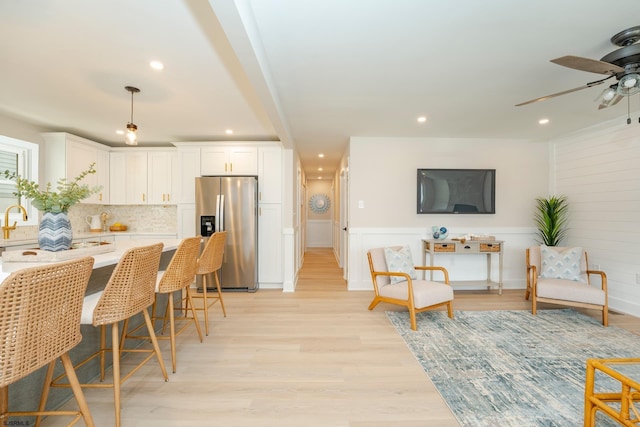 kitchen with stainless steel fridge with ice dispenser, backsplash, a breakfast bar area, white cabinets, and light wood-type flooring