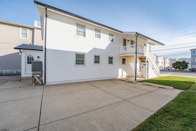 rear view of property with a yard, a balcony, central AC, and a patio area