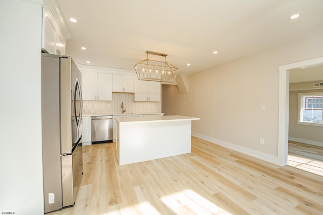 kitchen with stainless steel appliances, decorative light fixtures, light hardwood / wood-style flooring, white cabinets, and a kitchen island