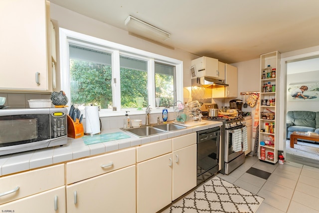 kitchen with gas stove, sink, black dishwasher, tile countertops, and white cabinets