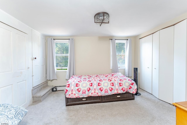 carpeted bedroom featuring a baseboard heating unit, multiple windows, and multiple closets