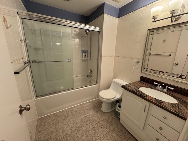 full bathroom with combined bath / shower with glass door, vanity, toilet, and tile walls