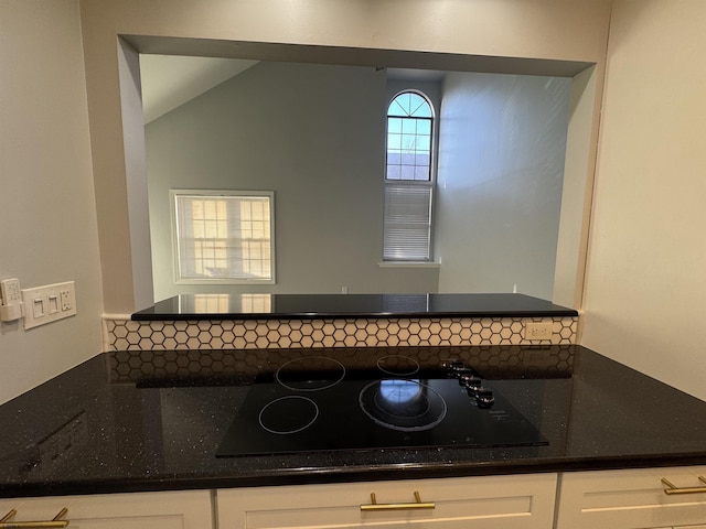 kitchen with black electric cooktop, lofted ceiling, dark stone countertops, and white cabinets