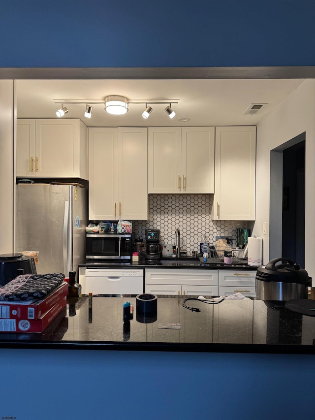 kitchen with dark stone countertops, stainless steel fridge, white dishwasher, decorative backsplash, and white cabinets