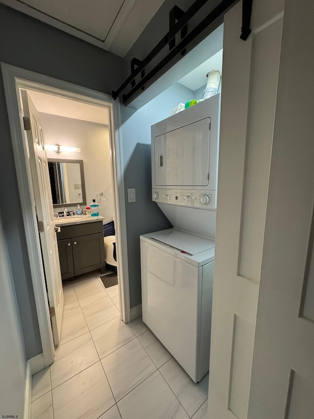 laundry area featuring a barn door, stacked washer and clothes dryer, sink, and light tile patterned floors