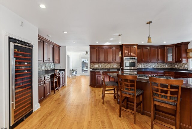 kitchen with pendant lighting, wine cooler, light wood-type flooring, double oven, and a breakfast bar area