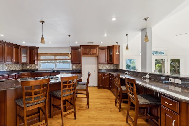 kitchen featuring tasteful backsplash, vaulted ceiling, pendant lighting, light hardwood / wood-style flooring, and a breakfast bar area