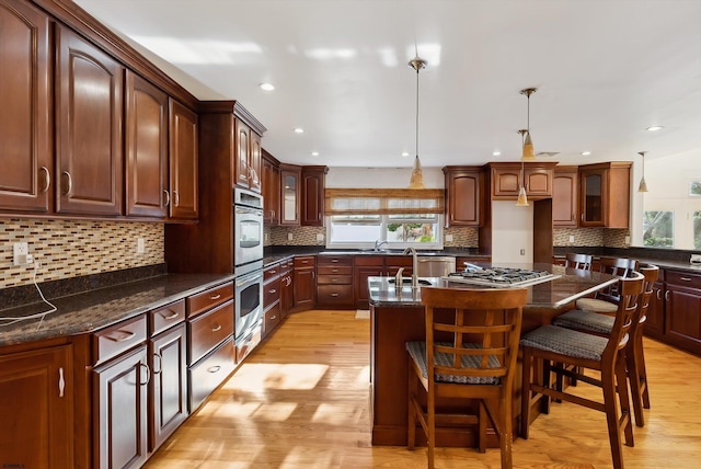 kitchen featuring hanging light fixtures, tasteful backsplash, light hardwood / wood-style floors, a kitchen bar, and a kitchen island with sink