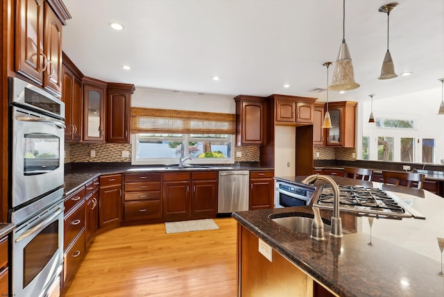 kitchen featuring decorative backsplash, stainless steel appliances, sink, pendant lighting, and light hardwood / wood-style floors