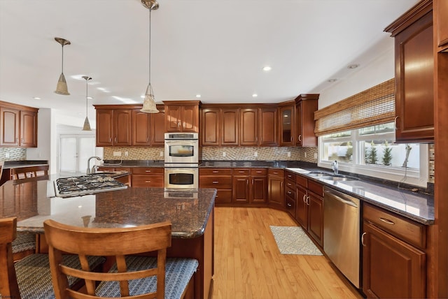 kitchen featuring appliances with stainless steel finishes, backsplash, light hardwood / wood-style flooring, and hanging light fixtures