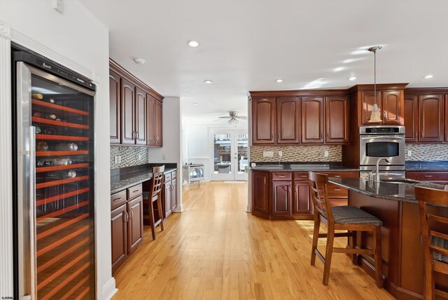 kitchen featuring hanging light fixtures, decorative backsplash, light wood-type flooring, stainless steel double oven, and beverage cooler