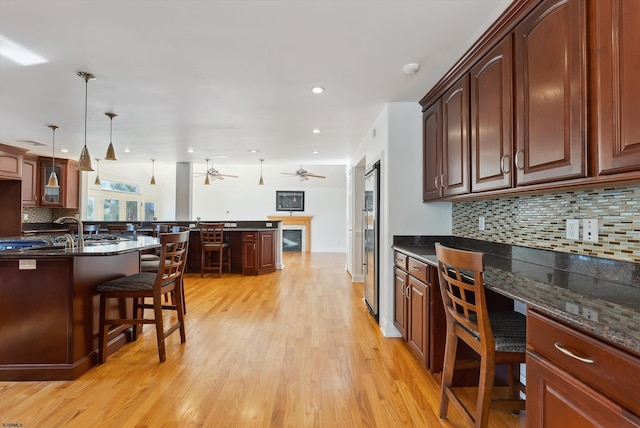 kitchen with ceiling fan, a kitchen breakfast bar, light hardwood / wood-style flooring, dark stone countertops, and decorative light fixtures