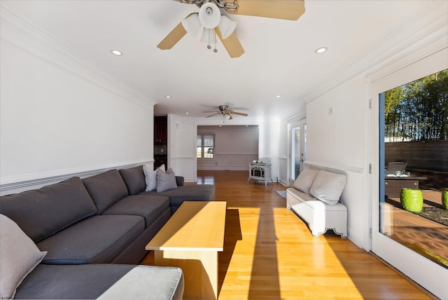 living room featuring ceiling fan, wood-type flooring, ornamental molding, and a wood stove