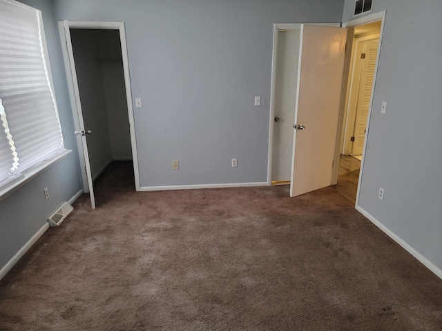 unfurnished bedroom featuring dark colored carpet, a spacious closet, and a closet