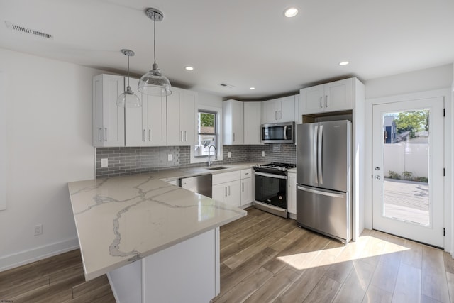 kitchen with appliances with stainless steel finishes, decorative light fixtures, and white cabinetry