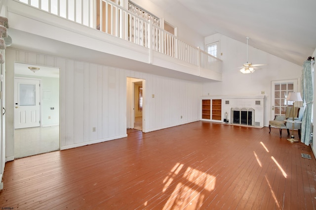 unfurnished living room featuring ceiling fan, a fireplace, a towering ceiling, and hardwood / wood-style flooring