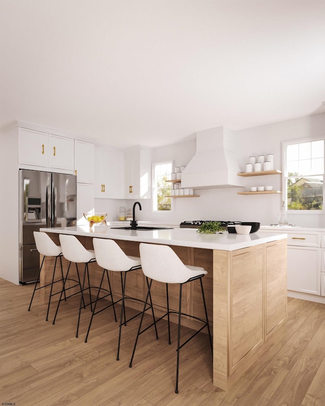 kitchen with white cabinets, custom range hood, and an island with sink