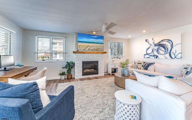 living room with ceiling fan, wood-type flooring, a wealth of natural light, and a brick fireplace