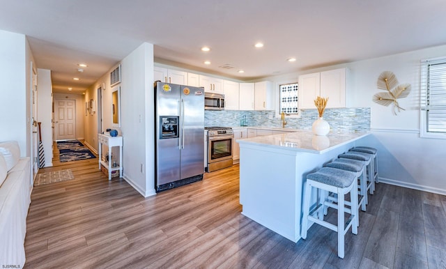 kitchen with white cabinets, a kitchen breakfast bar, light wood-type flooring, kitchen peninsula, and stainless steel appliances