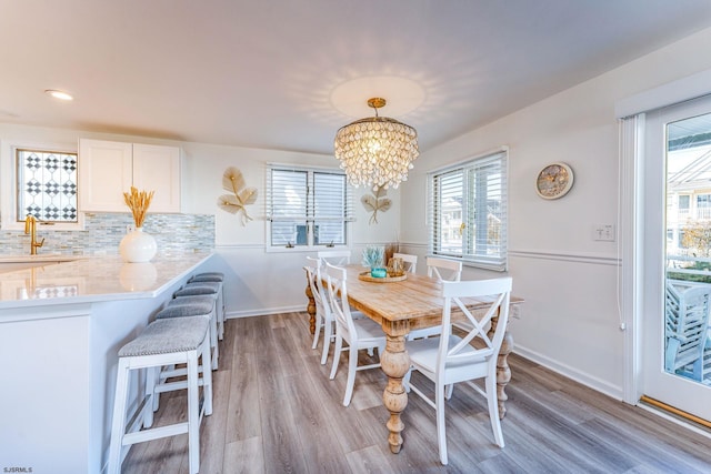 dining room featuring a healthy amount of sunlight, sink, light hardwood / wood-style floors, and an inviting chandelier