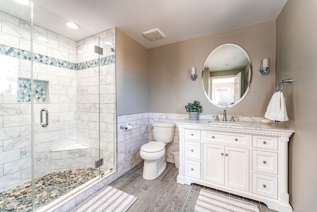 bathroom with vanity, toilet, a shower with door, and tile walls