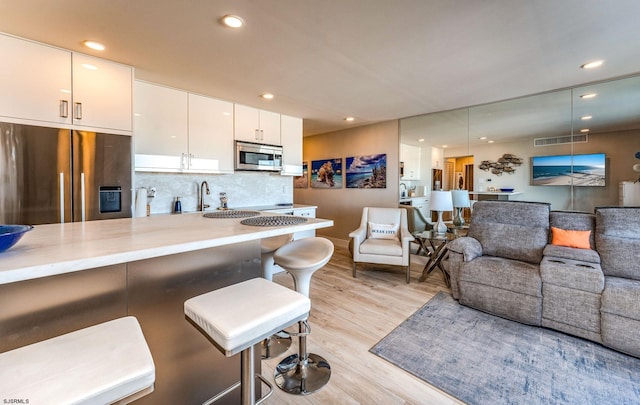 kitchen with appliances with stainless steel finishes, backsplash, a kitchen breakfast bar, light hardwood / wood-style flooring, and white cabinets