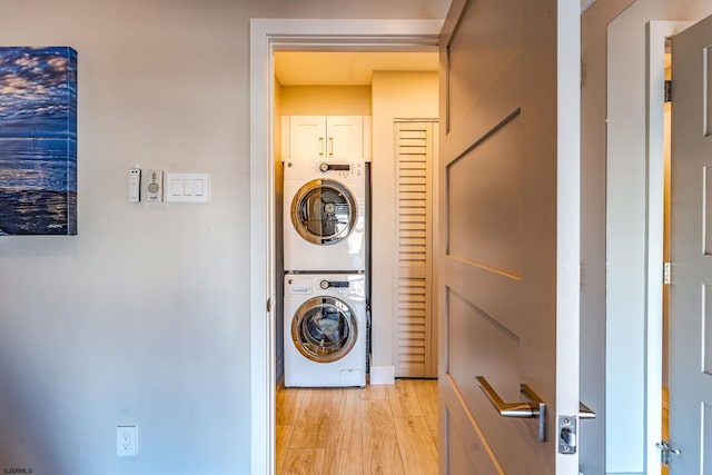 clothes washing area featuring cabinets, light wood-type flooring, and stacked washer and dryer