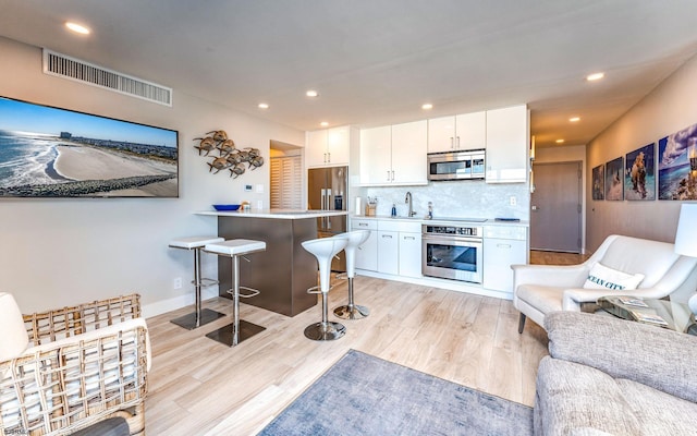 kitchen with white cabinetry, stainless steel appliances, tasteful backsplash, a kitchen bar, and light wood-type flooring