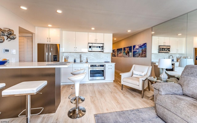 kitchen with a kitchen bar, stainless steel appliances, white cabinetry, and tasteful backsplash