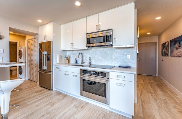 kitchen featuring sink, backsplash, stacked washer and dryer, white cabinets, and appliances with stainless steel finishes