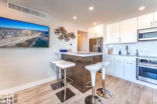 kitchen featuring appliances with stainless steel finishes, tasteful backsplash, sink, white cabinets, and a breakfast bar area