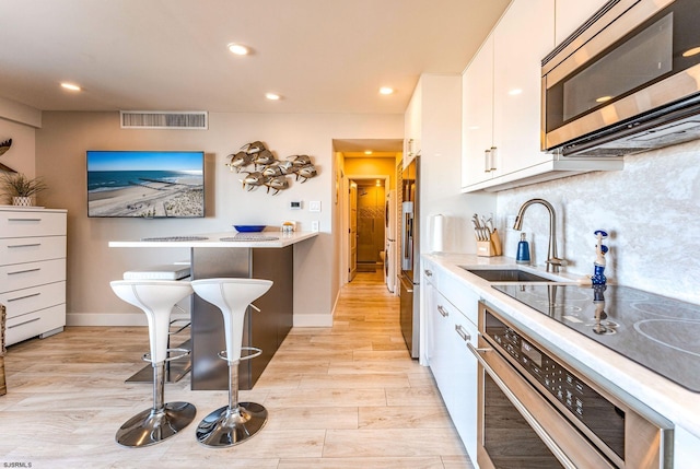 kitchen featuring a breakfast bar, stainless steel appliances, sink, light hardwood / wood-style flooring, and white cabinets