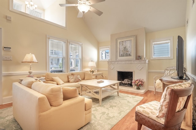 living room featuring a high ceiling, ceiling fan with notable chandelier, and light hardwood / wood-style floors