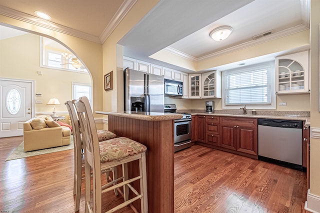 kitchen with a kitchen bar, ornamental molding, stainless steel appliances, and hardwood / wood-style flooring